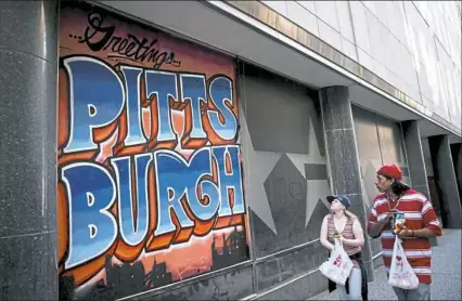  ?? Alex Driehaus/Post-Gazette ?? A couple walks past a mural painted on a boarded-up window on Wednesday at the former Macy’s building, Downtown.