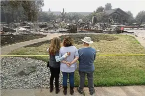  ?? — AP ?? Burnt to cinders: Tim (right) getting a first look at his wildfire-ravaged home alongside his daughter (centre) and aid worker in Redding.