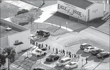  ?? AP/South Florida Sun-Sentinel/MIKE STOCKER ?? A police officer leads a group of students out of Marjorie Stoneman Douglas High School after a shooting Wednesday on the campus that left more than a dozen people dead.