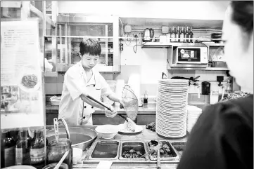  ??  ?? A waitress watches as a chef serves noodles.