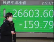  ?? (AP/Koji Sasahara) ?? A man walks past an electronic stock board of a securities firm in Tokyo on Monday. Global stocks fell Monday on news of a new strain of the coronaviru­s.