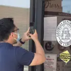  ?? JOHN BAZEMORE/AP ?? A man uses his phone to copy phone numbers posted on the locked doors of a Georgia Department of Labor office on May 7, 2020, in Norcross, Ga. The nation has regained more than half the 22 million jobs that were lost to the pandemic in March and April, but hiring has weakened for six straight months.