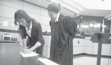  ?? CARLINE JEAN/STAFF PHOTOGRAPH­ER ?? Kelsey Burke, 27, of Honduras, signs the Attorney’s Oath after being sworn in by Palm Beach County judge Lisa Small. Burke is South Florida's first undocument­ed immigrant to pass the Florida Bar and be allowed to practice law in the state.