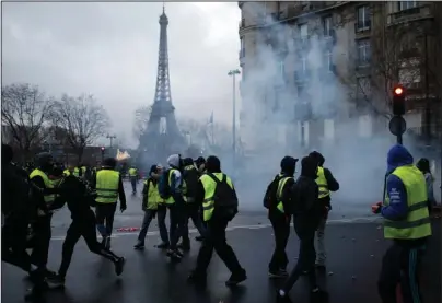  ?? The Associated Press ?? CENTRAL PARIS: Demonstrat­ors walk through tear gas during clashes Saturday in Paris. Crowds of yellow-vested protesters angry at President Emmanuel Macron and France’s high taxes tried to converge on the presidenti­al palace Saturday, some scuffling with police firing tear gas, amid exceptiona­l security measures aimed at preventing a repeat of last week’s rioting.