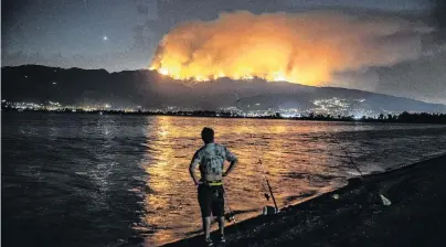  ??  ?? Holy smoke . . . Felipe Montiel, of San Marino, fishes at Lake Elsinore as the Holy fire reflects across the water while burning in the Cleveland National Forest above homes in Lake Elsinore, California, on Tuesday evening. The fastmoving fire broke out on Monday in the forest, burning more than 1600 hectares and forcing evacuation­s in two Orange County canyons.