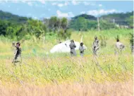  ?? NORMAN GRINDLEY/CHIEF PHOTO EDITOR ?? Members of the Jamaica Defence Force at the crash site of a Bell 206 helicopter in an open area near Phoenix Park in Portmore, St Catherine. Yesterday, a trainee pilot, who was the sole occupant, narrowly escaped major injuries after he was forced to make an emergency landing.