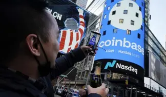  ?? ?? File-Coinbase employee Daniel Huynh holds a celebrator­y bottle of champagne as he photograph­s outside the Nasdaq MarketSite, in New York's Times Square