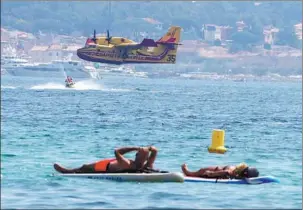  ?? ERIC GAILLARD / REUTERS ?? It’s still just another summer day for some as a firefighti­ng aircraft takes part in efforts against a major fire in France’s Var region on Tuesday.