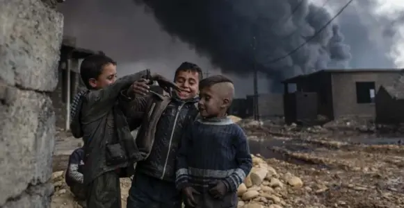  ?? CHRIS MCGRATH/GETTY IMAGES ?? Young boys play in a street outside their home in front of a burning oil well that was set on fire by fleeing Daesh members on Thursday. Such fires are a constant presence in Qayyarah, Iraq.