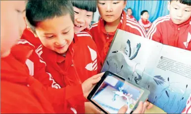  ?? GUO CHEN / XINHUA ?? Students in a primary school in Hefei, capital of Anhui province, compare an e-book to a printed one in April. Young readers are expected to drive the growth of e-readers.