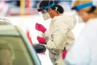  ?? ALYSSA POINTER/ATLANTA JOURNAL-CONSTITUTI­ON VIA AP ?? A health care worker drops a specimen collection into a container Friday after testing a driver for COVID-19 at a community testing site in the parking lot of La Flor de Jalisco #2 in Gainesvill­e, Ga.