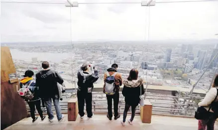  ??  ?? Visitors on the viewing platform of Seattle’s Space Needle look east through newly installed glass panels. Recently completed renovation­s on the 56-year-old landmark include the installati­on of floor-to-ceiling glass on the viewing deck and a glass floor to the rotating restaurant. Total cost of the project was $100 million.