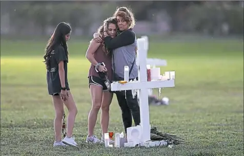  ?? Gerald Herbert/Associated Press ?? People hug as they pay homage Friday at the memorial crosses for the 17 deceased students and faculty from the Wednesday shooting at Marjory Stoneman Douglas High School in Parkland, Fla.