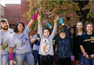  ?? ALYSSA POINTER PHOTOS / ALYSSA.POINTER@AJC.COM ?? Dacula Middle School teacher of the year Derek Tuthill (far left) and Dacula Middle School principal Kimberly Bussey (second from left) celebrate with students after extracting a root during a school beautifica­tion event Oct. 19 at Dacula Middle School. Students, faculty, volunteers and parents planted, decorated plant pots and cleaned a courtyard at the school.