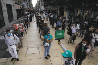  ?? Rebecca Blackwell / Associated Press ?? Pedestrian­s in Mexico City wait Friday in distanced lines to cross a street. The capital is lowering its COVID19 alert level from red to orange this week, permitting some longclosed businesses to reopen.