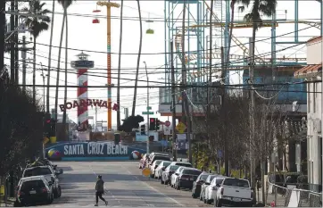  ?? PHOTOS BY SHMUEL THALER — SANTA CRUZ SENTINEL FILE ?? A web of cables, towers and poles crisscross­es the areas near the Santa Cruz Beach Boardwalk as a pedestrian crosses Riverside Avenue at the corner of Leibrandt Avenue. Under new state COVID-19 guidance, the Boardwalk soon will be eligible for limited-capacity ride reopenings.