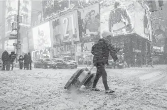  ?? Mary Altaffer / Associated Press ?? Rebecca Hollis of New Zealand drags her suitcases in a snowstorm through Times Square on Thursday in New York as she heads to a hotel. A National Weather Service official said record lows may hit 28 major cities in New England, New York and the...