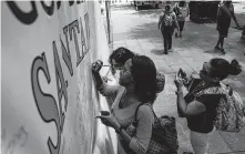  ?? Michael Ciaglo / Houston Chronicle ?? Tasha Baylor, center, signs a banner for victims of the Santa Fe High School shooting at Discovery Green Park.