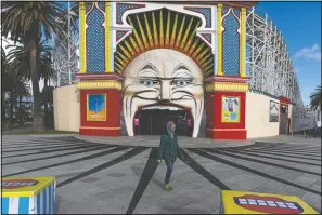  ??  ?? A man wearing a mask walks Wednesday past Luna Park in the suburb of St. Kilda during lockdown in Melbourne, Australia People are allowed to exercise for one hour a day within a 5-kilometer radius of their house. Victoria, Australia’s coronaviru­s hot spot, announced Monday businesses will be closed and scaled down in a bid to curb the spread of the virus.