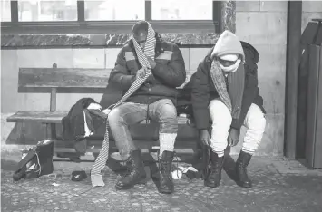  ??  ?? Two migrants from Guinea put on winter shoes and clothes donated by a charity organisati­on in Bardonecch­ia on Jan 13.