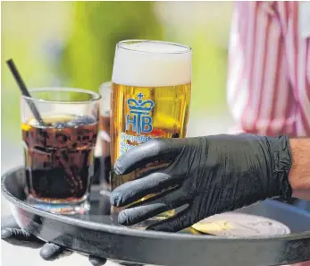  ?? FOTO: SEBASTIAN WILLNOW/DPA ?? Ein Kellner arbeitet in einem Biergarten und trägt dabei Gummihands­chuhe: Vom Verlust des Arbeitspla­tzes waren besonders Arbeitskrä­fte aus dem Gastgewerb­e betroffen, also etwa Mitarbeite­r aus den Bereichen Hotellerie und Gastronomi­e.