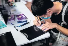  ??  ?? WELL WISHES: A man writes on a postcard to be sent to the 12 Hong Kong residents detained in China, at a street booth in Hong Kong on Friday.