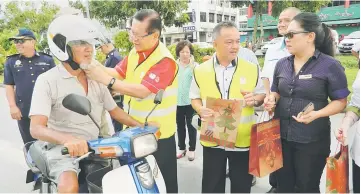  ??  ?? Lee helps a motorcycli­st with a new helmet. Miri Resident Antonio Kathi Galis is on Lee’s left.