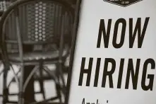  ?? Olivier Douliery / Getty Images ?? A restaurant displays a “Now Hiring” sign. Since service-sector jobs now mean a higher chance of coronaviru­s infection, even higher pay isn’t coaxing enough workers.