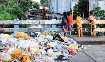  ?? GEORGE CALVELO/AFP ?? A pile of rubbish, including plastic waste, is seen as children play on a bridge in downtown Manila.