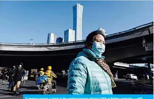  ?? —AFP ?? A woman crosses a street in the central business district (CBD) of Beijing yesterday.