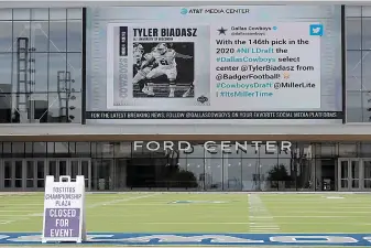  ?? AP Photo/Tony Gutierrez ?? ■ A sign sits on an artificial field frequented by fans at the Ford Center by The Star, the Dallas Cowboys headquarte­rs and training facility, as a large video screen on the exterior wall of the building broadcast the team’s latest selection in the NFL football draft Saturday in Frisco, Texas.