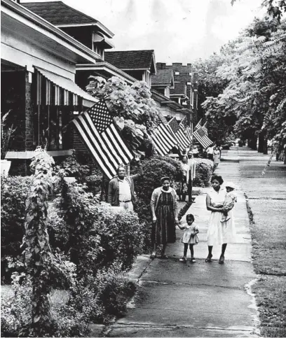  ?? GEORGE QUINN/CHICAGO TRIBUNE ?? Above, flags fly from every house in the 7100 block of South Wabash Avenue on July 4, 1961. In the foreground are, from left, Mr. Elmer Myer, Mrs. Sybil Myer, and Mrs. Ernest Wash with her children Paula, 2, and Lonnie, 1. Myer was a veteran and the vice president of the block club responsibl­e for the flags.