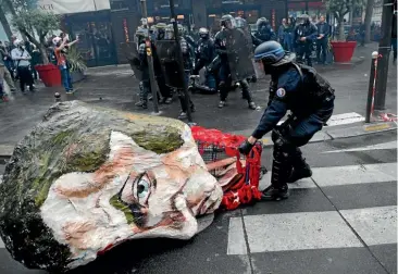  ?? AP ?? A riot police officer removes a huge mask of French President Emmanuel Macron during a demonstrat­ion in Paris yesterday.