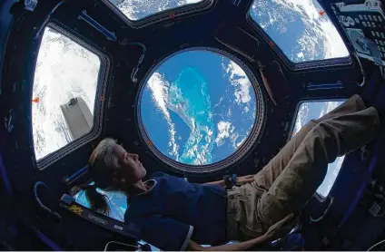  ?? NASA / AFP via Getty Images ?? Shannon Walker looks out of the Internatio­nal Space Station’s cupola at the Caribbean view beneath on Nov. 25, 2010.