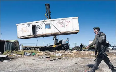  ?? Abir Sultan European Pressphoto Agency ?? IN THE WEST BANK, an Israeli border police officer this month passes the outpost of Amona during the court-ordered demolition.