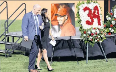  ?? AP PHOTO ?? Brandy Halladay, wife of late MLB pitcher Roy Halladay, walks looks at a photograph of her husband while escorted back to her seat by Emcee and Phillies announcer Tom McCarthy during a Celebratio­n of Life for Roy Halladay at Spectrum Field in...