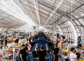  ?? JUSTIN KANEPS / THE NEW YORK TIMES ?? Workers assemble Model 3s in a heavy-duty tent at Tesla’s factory in Fremont, Calif. The company built the tent just so it could make more Model 3s.