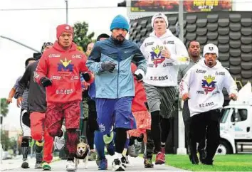  ?? AFP ?? Dogs of war Following an escort on a bicycle, boxer Manny Pacquiao (centre) is joined by supporters and training mates on his morning jog along a city street to a park in Los Angeles.