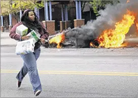  ?? SHANNON STAPLETON / REUTERS ?? A woman with goods looted from a store runs past burning vehicles. Looting broke out at a mall northwest of downtown Baltimore during the unrest.