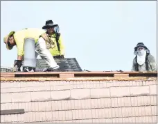  ?? Westside Eagle Observer/MIKE ECKELS ?? Three workers, wearing protective gear, strip off the old roofing material on Decatur High School’s Peterson Gym on June 22. A hail storm in October 2019 significan­tly damaged the roof enough that water leaked in several locations on the basketball court, damaging the floor.