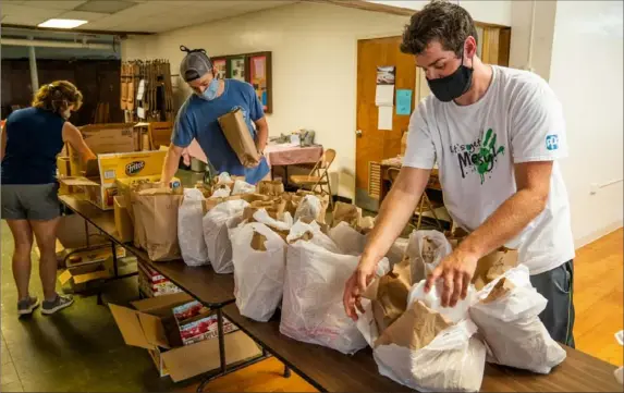  ?? Andrew Rush/Post-Gazette photos ?? Ryan McIntyre, center, and Andy Snyder, both of the North Hills, pack bags of food for North Hills Cares, a nonprofit founded by North Hills parents to help kids in need on July 29 in West View. The organizati­on provides two days’ worth of meals on Mondays, Wednesdays and Fridays, plus a weekend “backpack” of food.