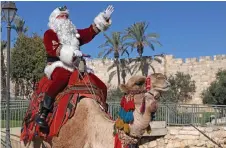  ?? — AFP photo ?? Kassissieh, dressed as Santa Claus, poses for a picture as he rides a camel at Jaffa Gate in Jerusalem’s Old City, a few weeks before the upcoming holiday of Christmas.