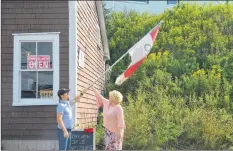  ?? KIRK STARRATT ?? Craig Parker and Madonna Spinazola hang the “open” flag as Parker’s General Store in Halls Harbour is officially reopened