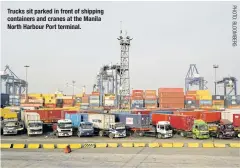  ??  ?? Trucks sit parked in front of shipping containers and cranes at the Manila North Harbour Port terminal.