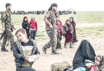  ?? — AFP ?? Fighters with the Us-backed Syrian Democratic Forces walk past civilians at a screening area for those who are evacuated from the IS group’s embattled holdout of Baghouz, during an operation to expel IS militants from the area, in the eastern Syrian province of Deir Ezzor, on Tuesday.