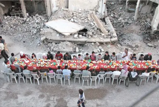  ??  ?? Residents of the Syrian town of Douma, on the outskirts of Damascus, break their fast with the iftar meal on a heavily damaged street. (AFP)