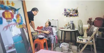  ??  ?? (Above) Chan Lai (centre), who is in her mid 80s, thanks Paul Pun, who heads the Macau branch of global charity Caritas, after he gave her a food box in her flat in Macau. • (Below) Paul speaks to a colleague on his phone as he tries to help an elderly...