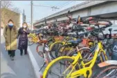  ?? ZHAO RONG / FOR CHINA DAILY ?? Two pedestrian­s walk past shared bikes that are randomly piled by the side of a road in Beijing in January.