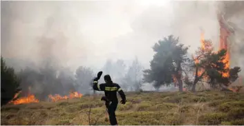  ?? — Reuters ?? A firefighte­r walks on a field as flames rise during a wildfire near the village of Kapandriti, north of Athens, on Tuesday.