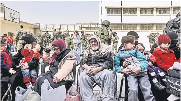  ??  ?? Evacuated civilians sitting in the yard of a school lying on the government side of the Wafideen checkpoint on the outskirts of the Syrian capital Damascus neighbouri­ng the Eastern Ghouta enclave, with Syrian and Russian soldiers along with members of...